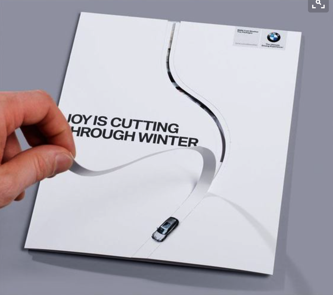 hand pulling a strip of paper from a printed direct mail piece for bmw, the line leaves a trace behind the car making it look like a track in the snow